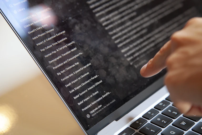 A hand seen at a laptop pointing to the screen.