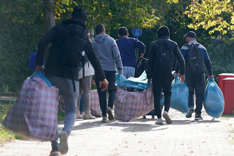 People with luggage walk down a road.