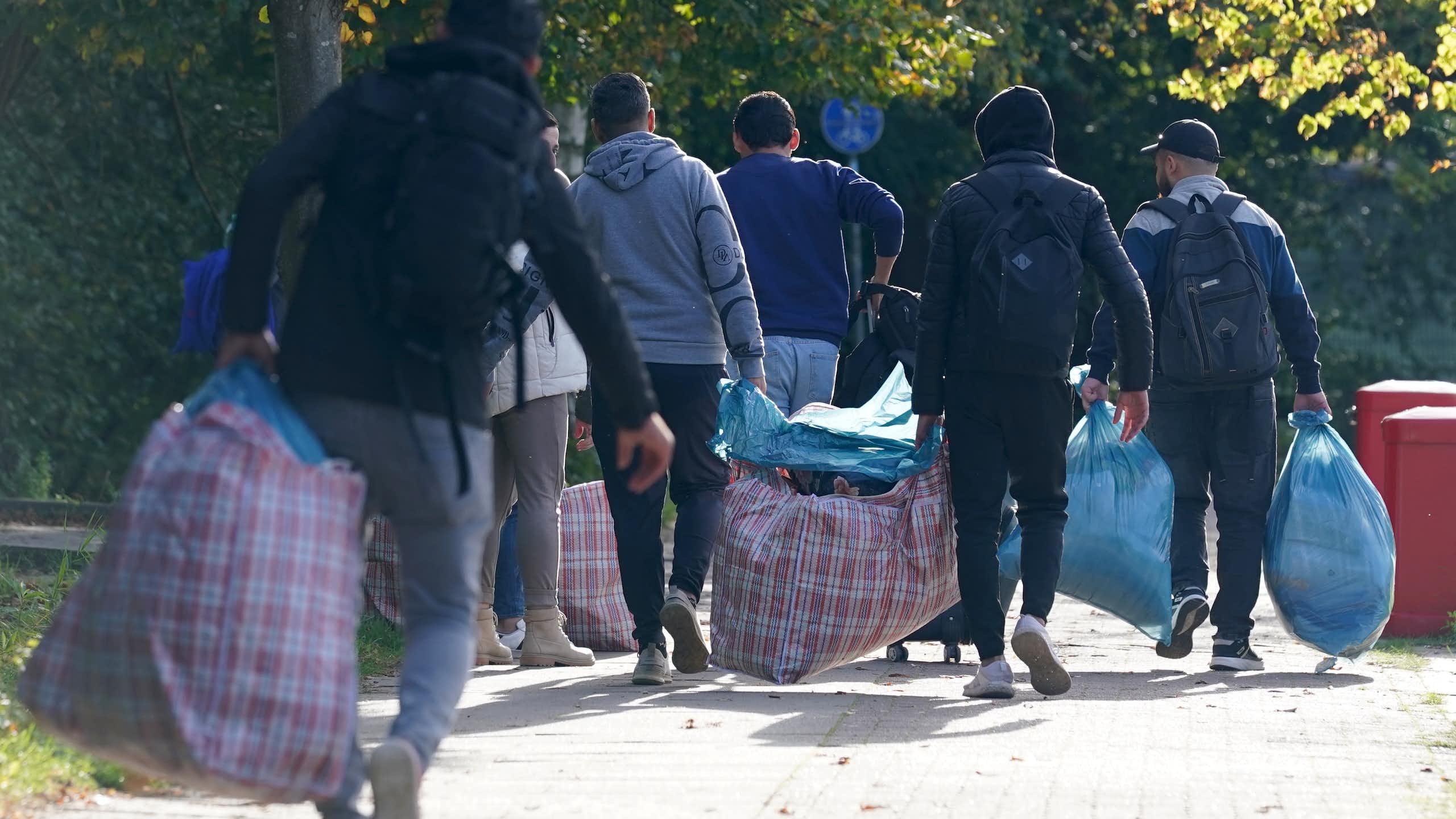 People with luggage walk down a road.