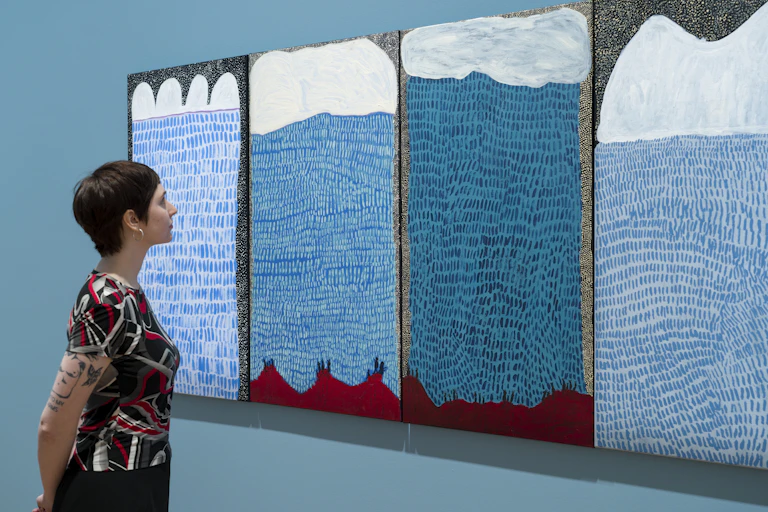 A woman looks at blue paintings