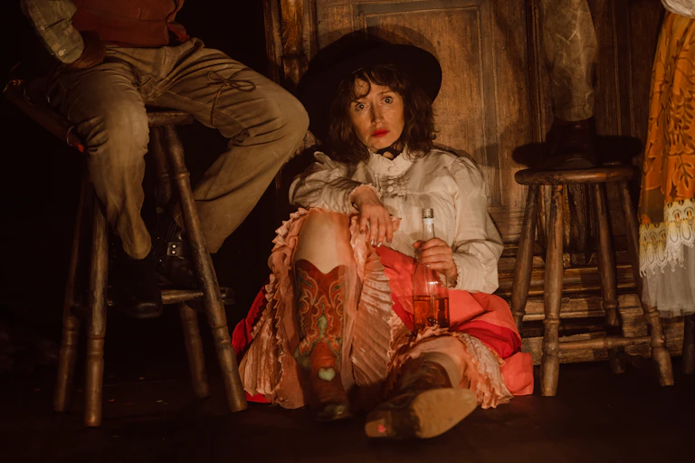 A cowgirl sits on the floor with a bottle of booze.