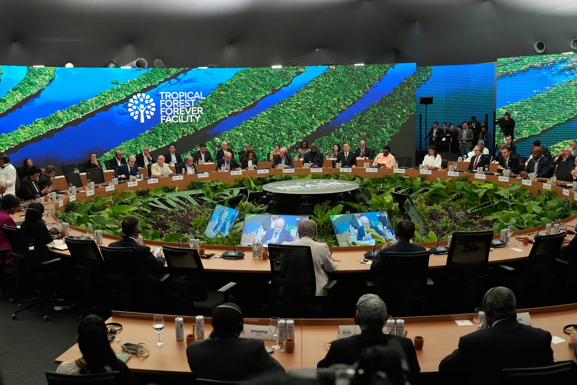 A group of delegates sit around a round table with forest images in the background.