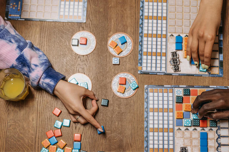 Three hands and a board game are viewed from the top.