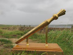 A man in a blue jacket stands in the open doorway of a stone building.