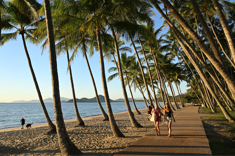 People are seen walking along the beach as the sun rises over Palm Cove, north of Cairns in Queensland