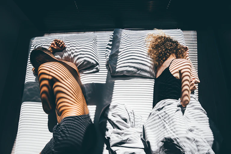 Male and female couple sleeping in bed, backs to each other, women with sheet over her, man without