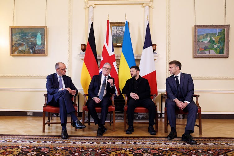 Friedrich Merz, Keir Starmer, Volodymyr Zelenskyy and Emmanuel Macron sitting in front of their national flags.