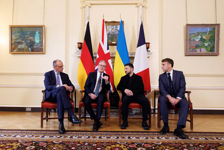 Friedrich Merz, Keir Starmer, Volodymyr Zelenskyy and Emmanuel Macron sitting in front of their national flags.