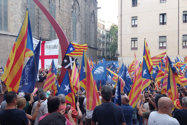 A group of people with Aliança Catalana flags gathered in a square