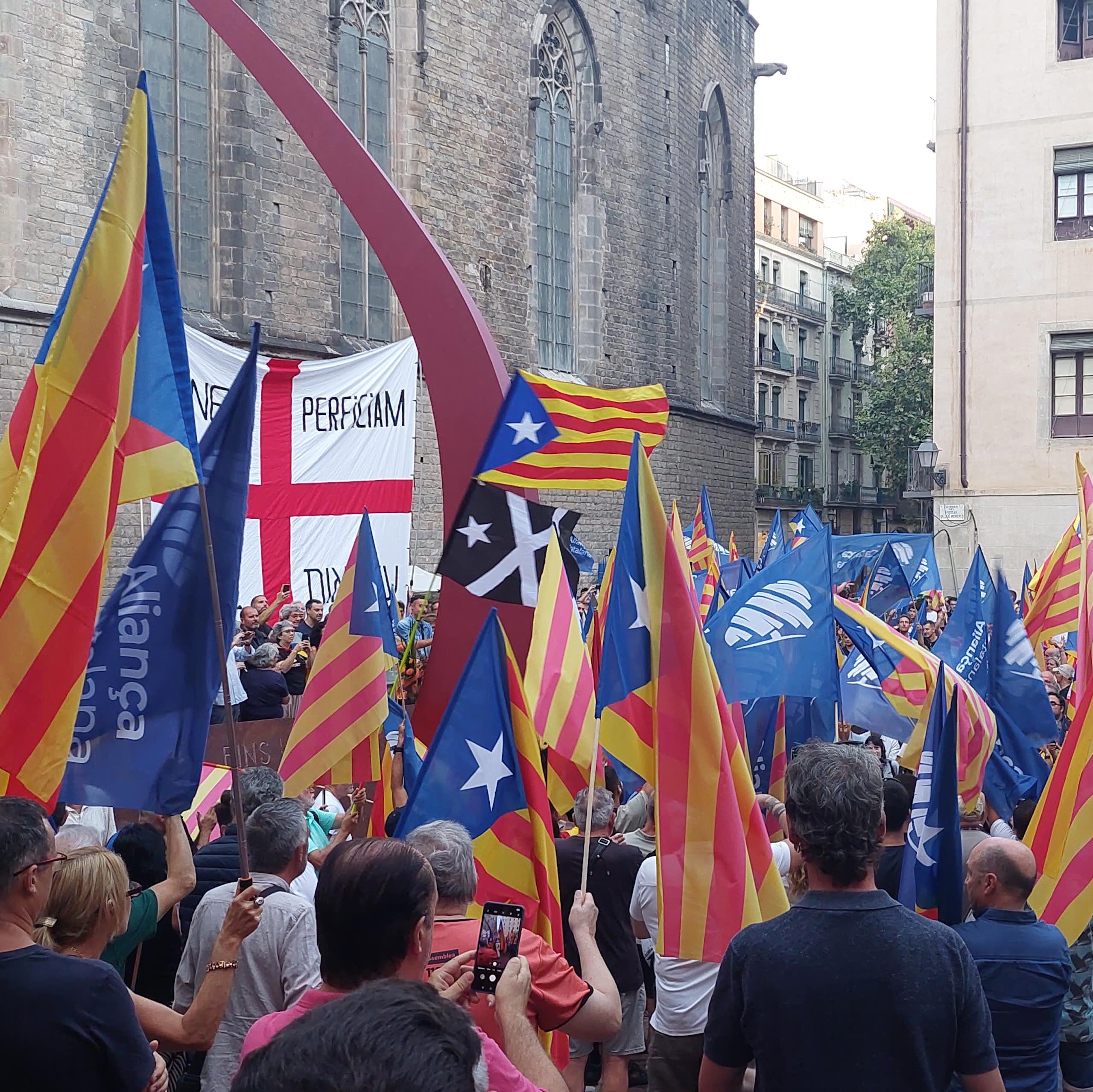 A group of people with Aliança Catalana flags gathered in a square