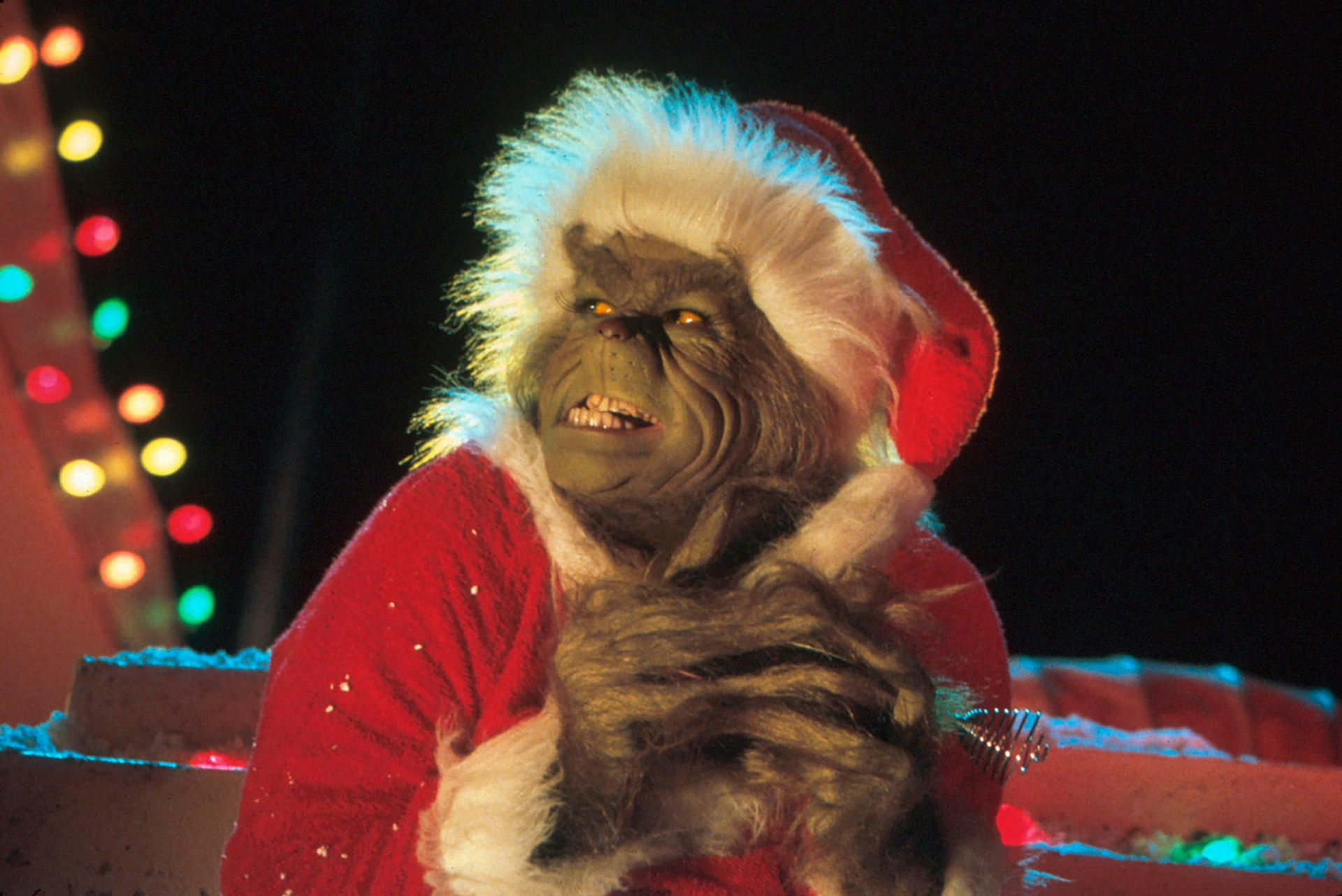 A movie still of Jim Carrey as The Grinch, wearing a red Santa hat and grinning diabolically.