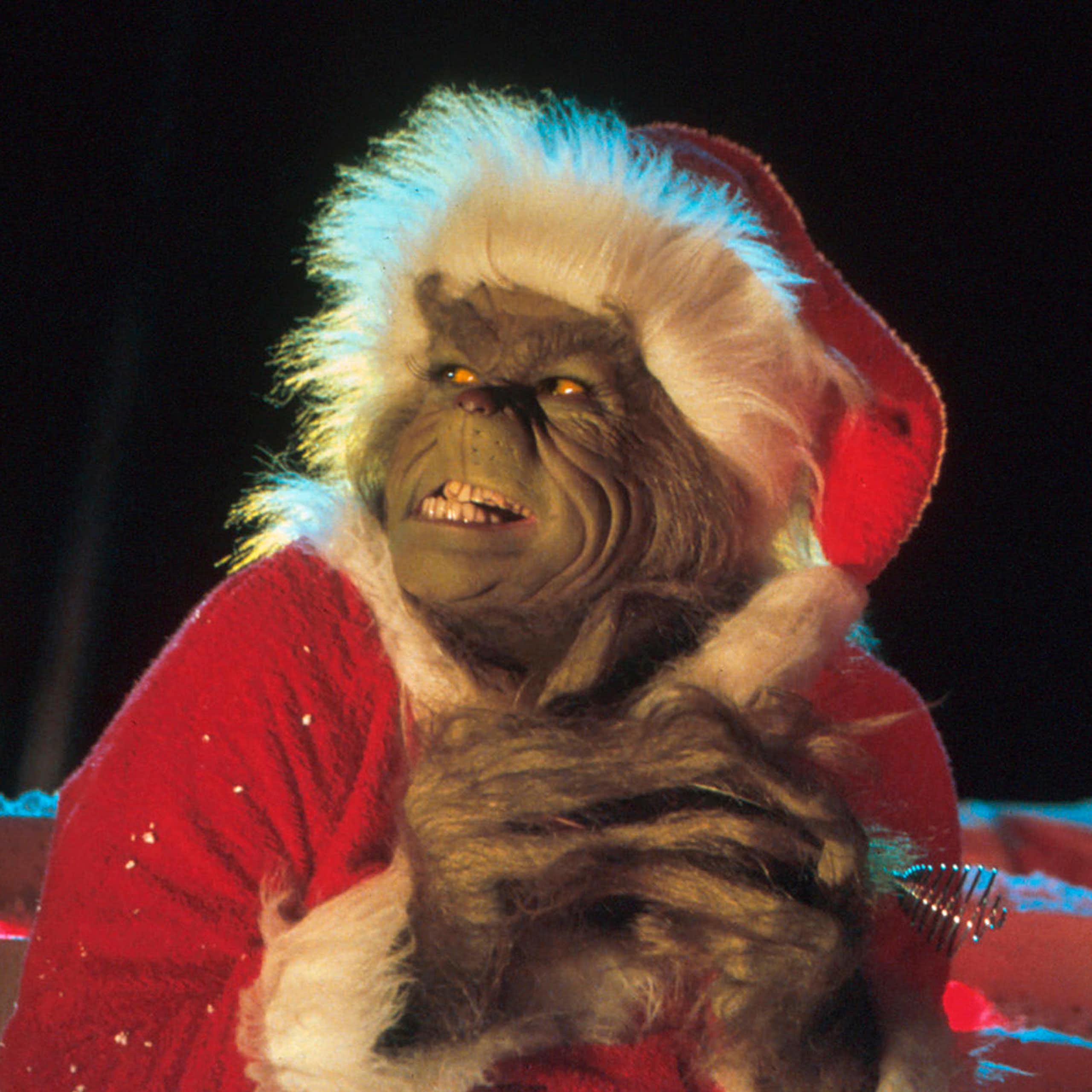 A movie still of Jim Carrey as The Grinch, wearing a red Santa hat and grinning diabolically.