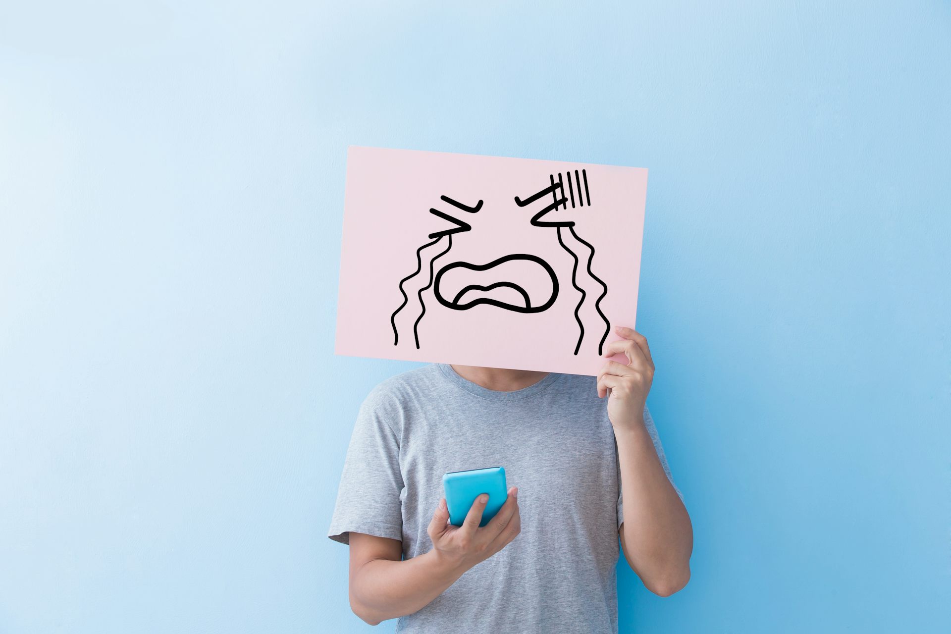 Un hombre con móvil se tapa la cara con una cartulina con el dibujo de alguien llorando.