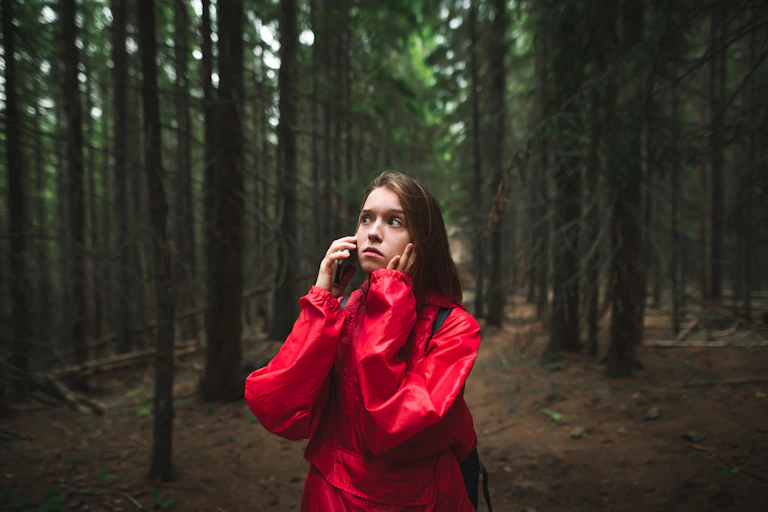 Scared young female tourist in red raincoat is lost in forest.
