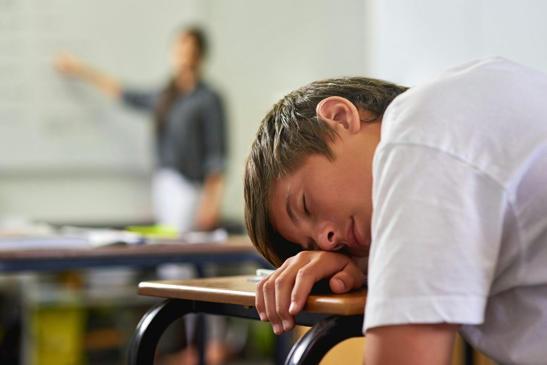 Un adolescente dormido sobre el pupitre de clase.