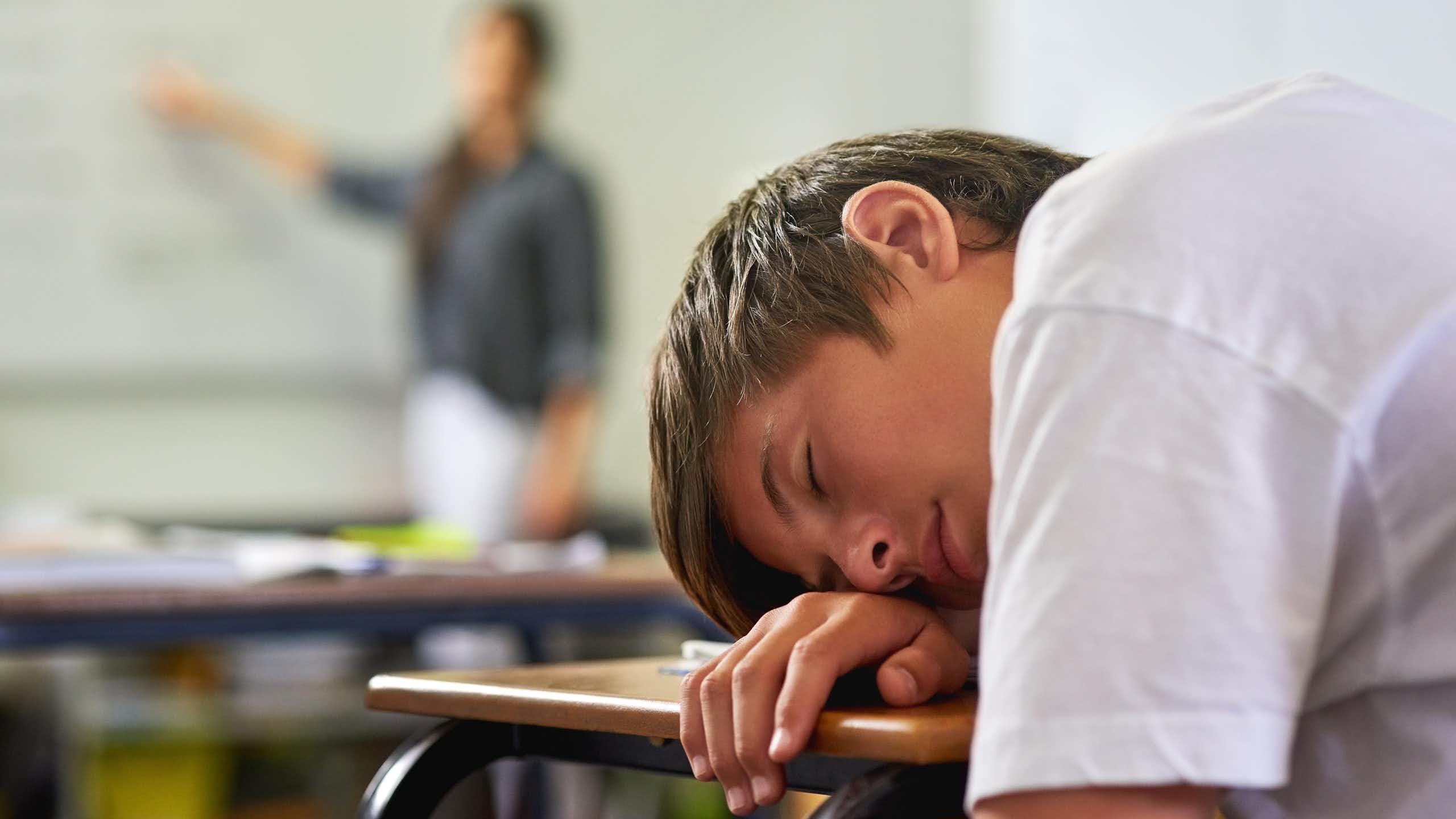 Un adolescente dormido sobre el pupitre de clase.