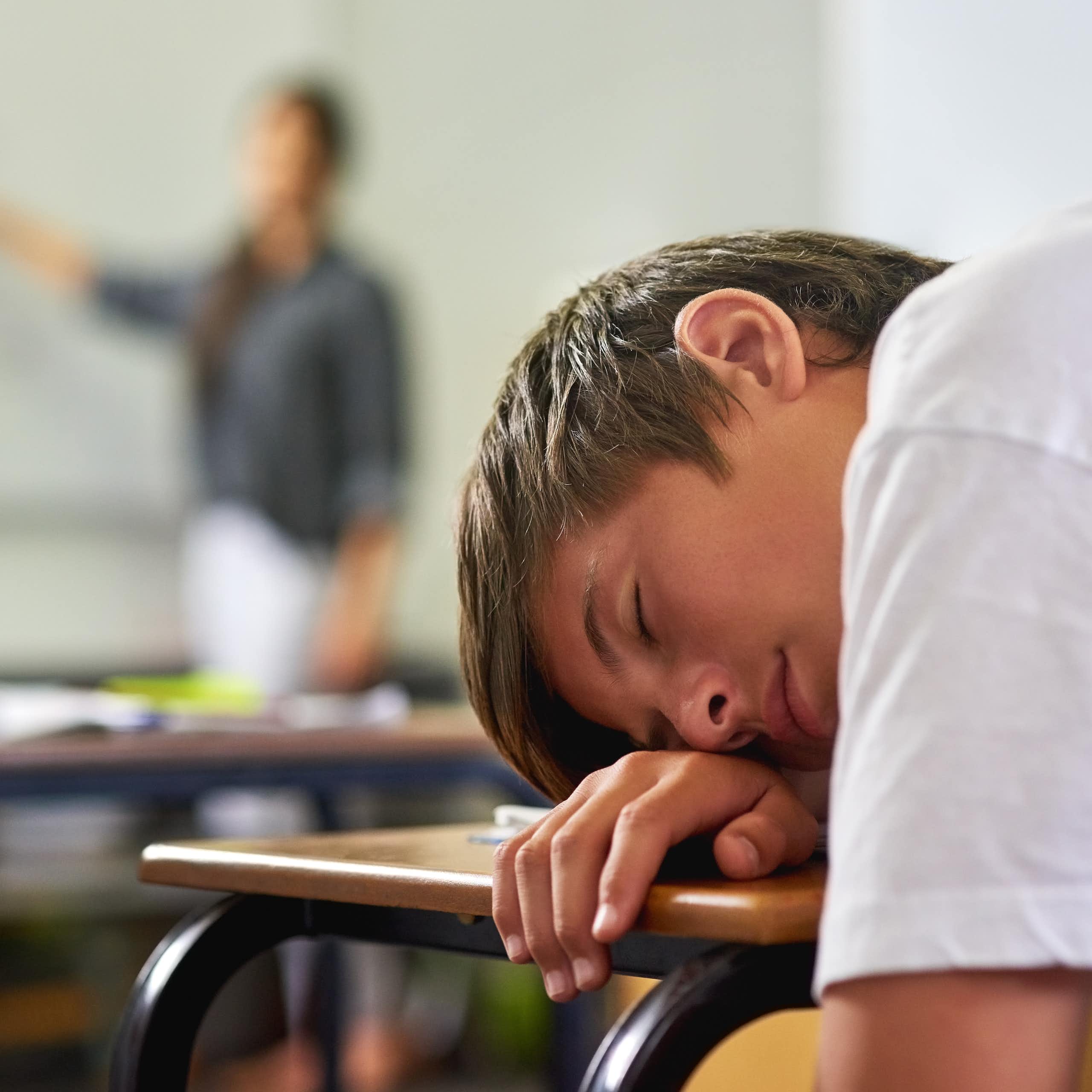 Un adolescente dormido sobre el pupitre de clase.