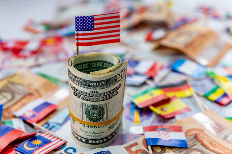 A computer-generated image showing a US flag sticking out of a wad of dollars with other flags lying in the background.