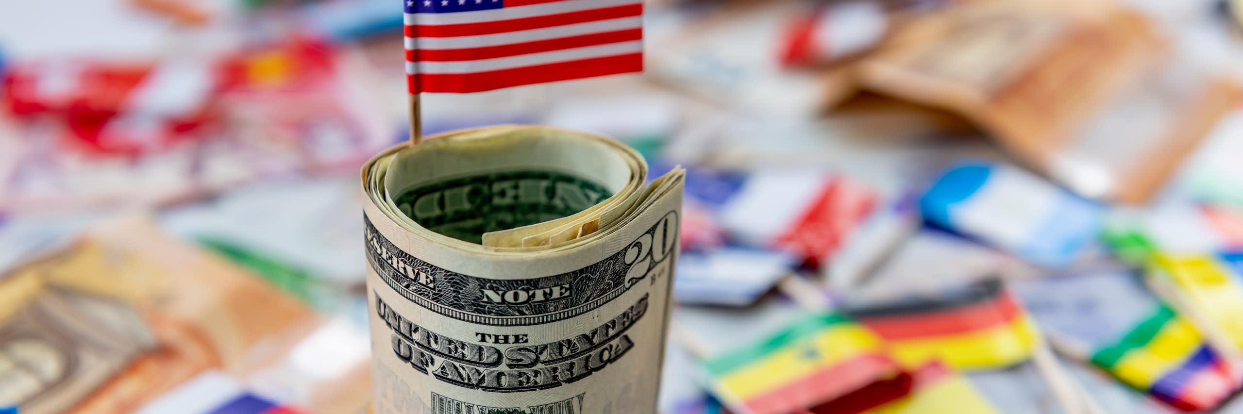 A computer-generated image showing a US flag sticking out of a wad of dollars with other flags lying in the background.