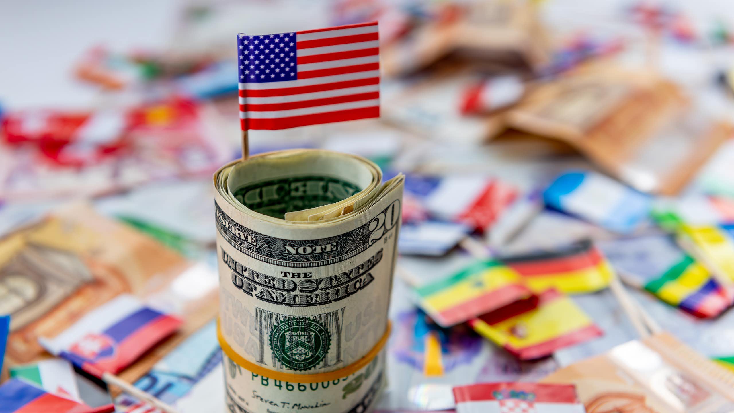 A computer-generated image showing a US flag sticking out of a wad of dollars with other flags lying in the background.