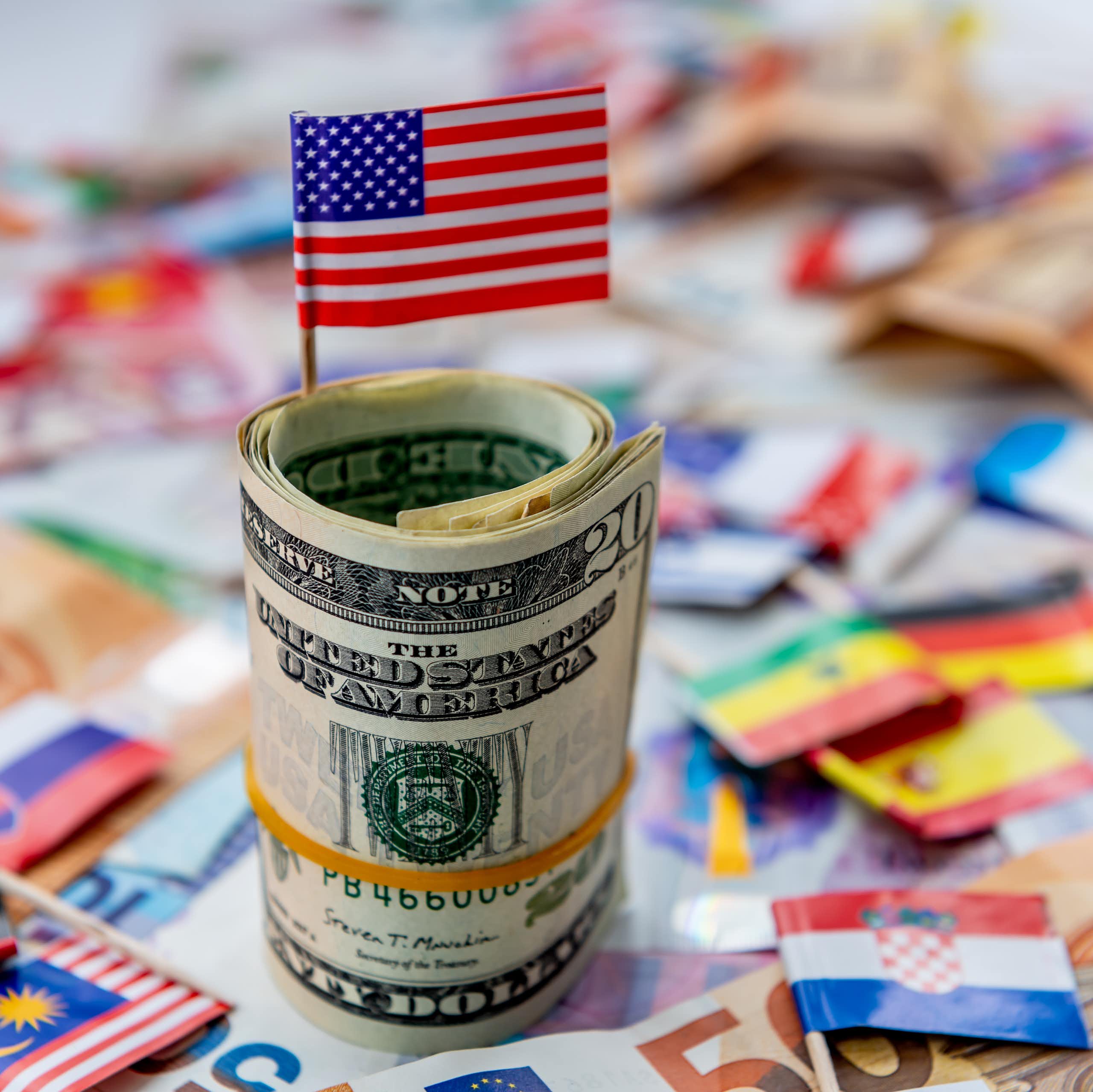 A computer-generated image showing a US flag sticking out of a wad of dollars with other flags lying in the background.