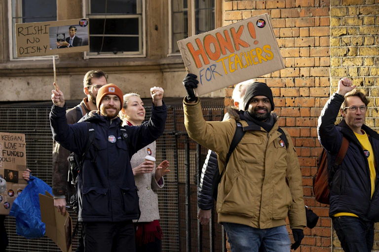 striking teachers on a picket line with one holding up a sign saying honk for teachers