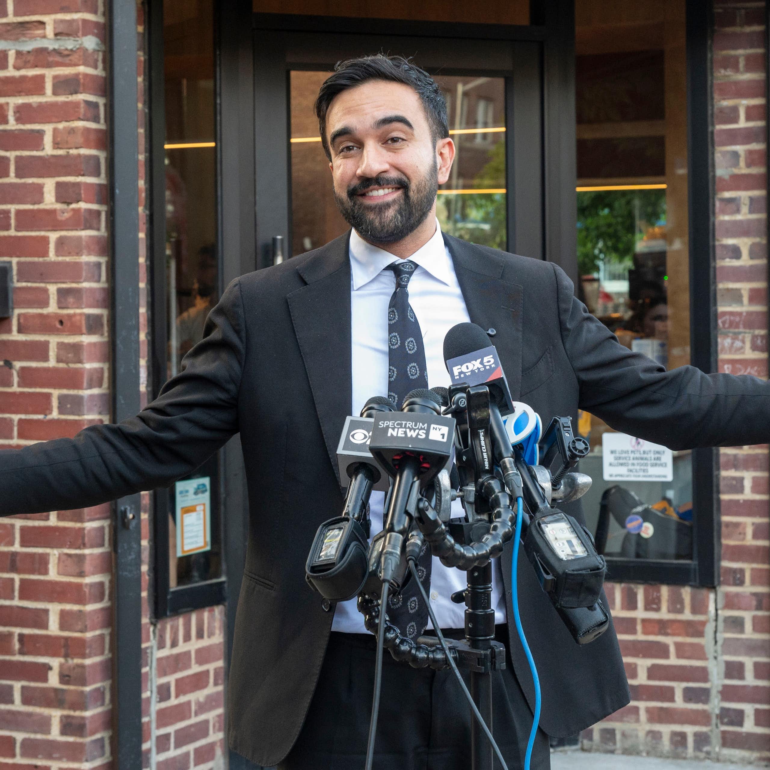 Un hombre con traje abre los brazos ante varios micrófonos.