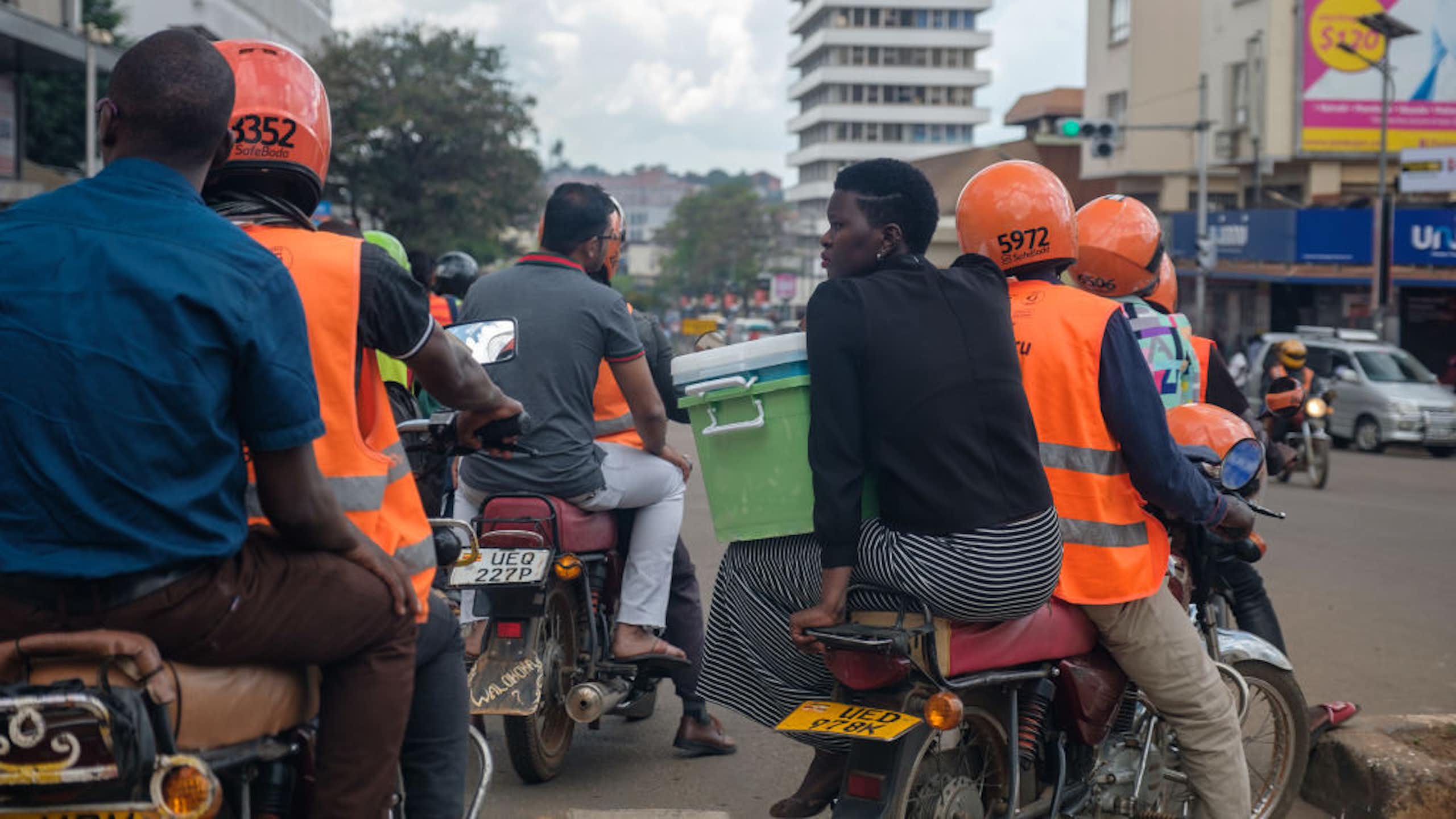 People in orange vests and helmets driving motorbikes with passengers on a city street