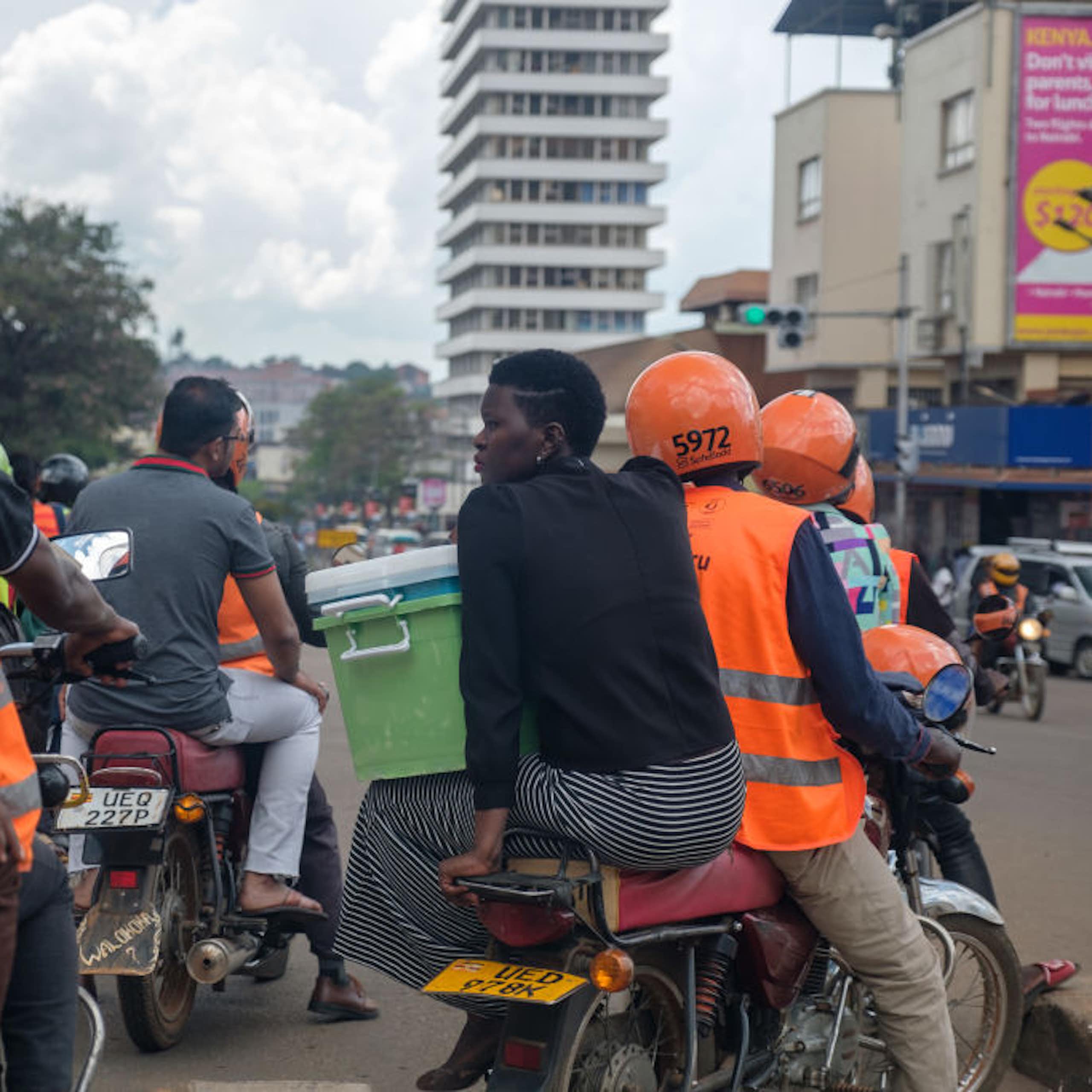 People in orange vests and helmets driving motorbikes with passengers on a city street
