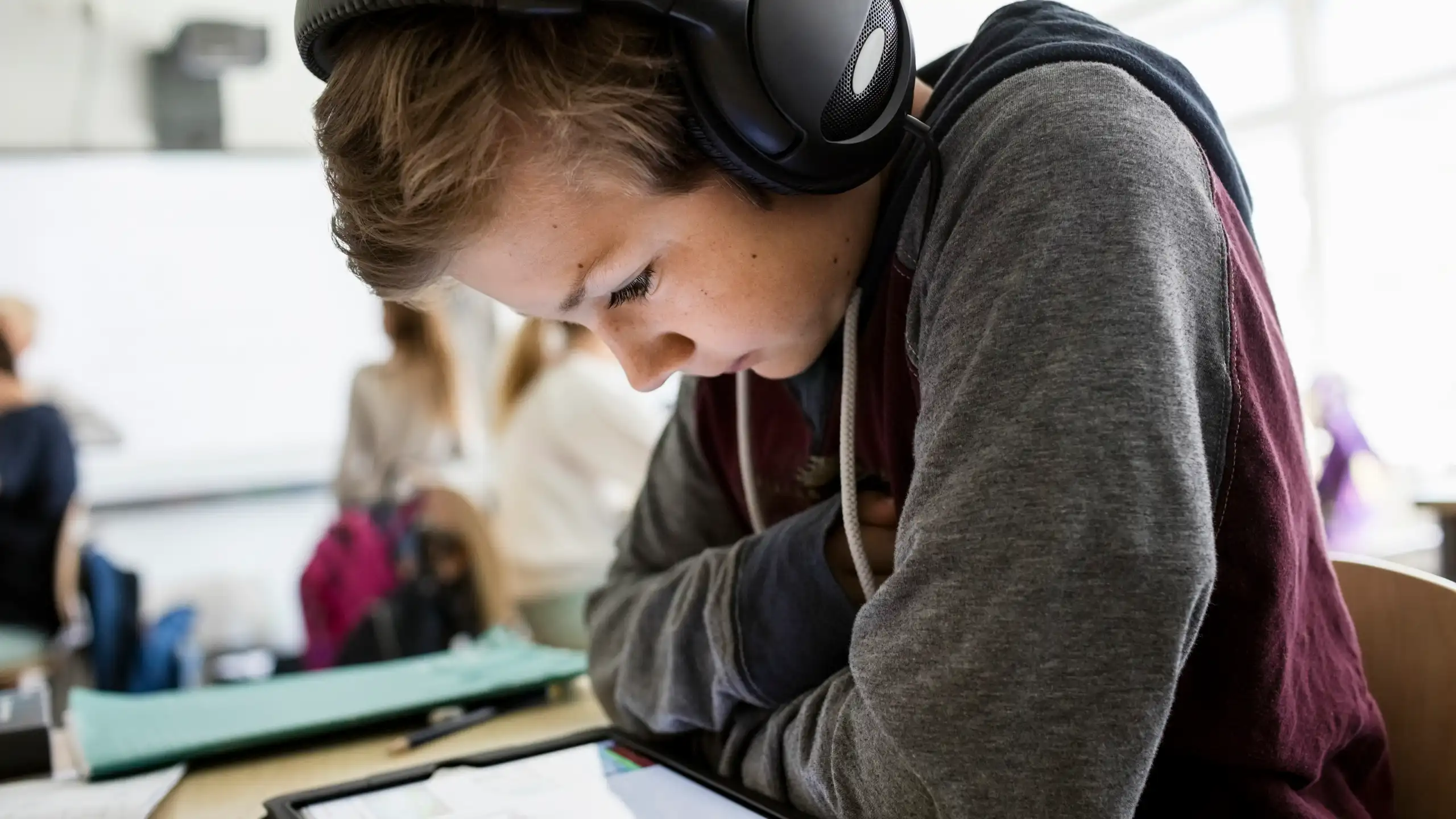 Boy sitting in classroom looking at tablet with headphones on.