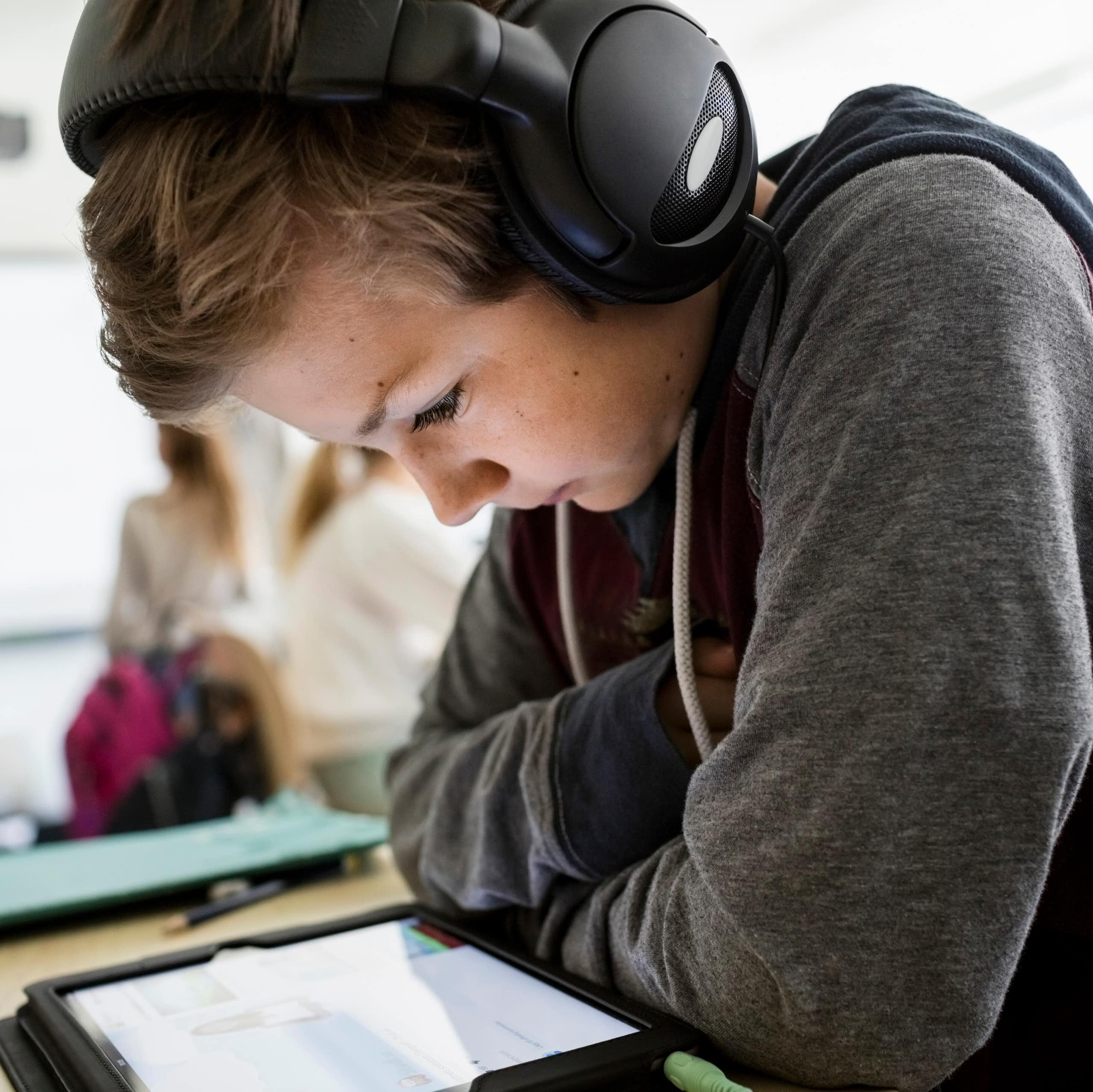 Boy sitting in classroom looking at tablet with headphones on.