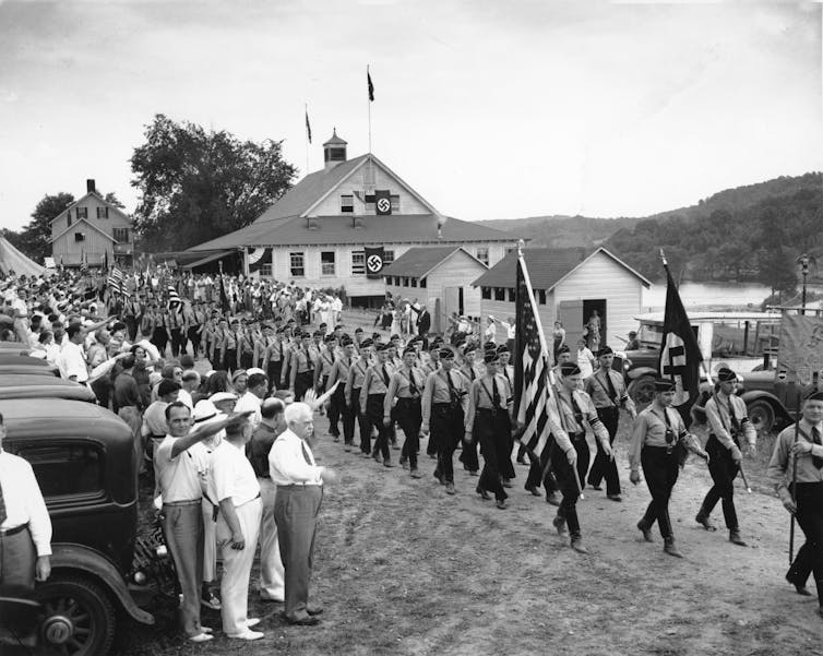 Hundreds of American Nazis walk on a country road.