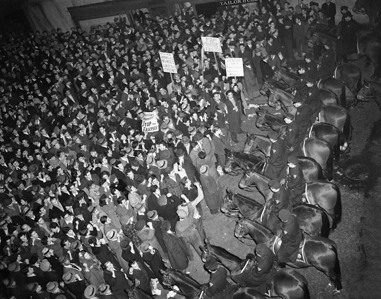 Mounted police form a line in front of hundreds of people.