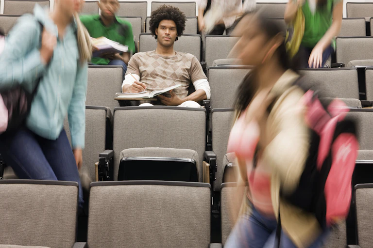 College student sitting in lecture hall while others walk around.