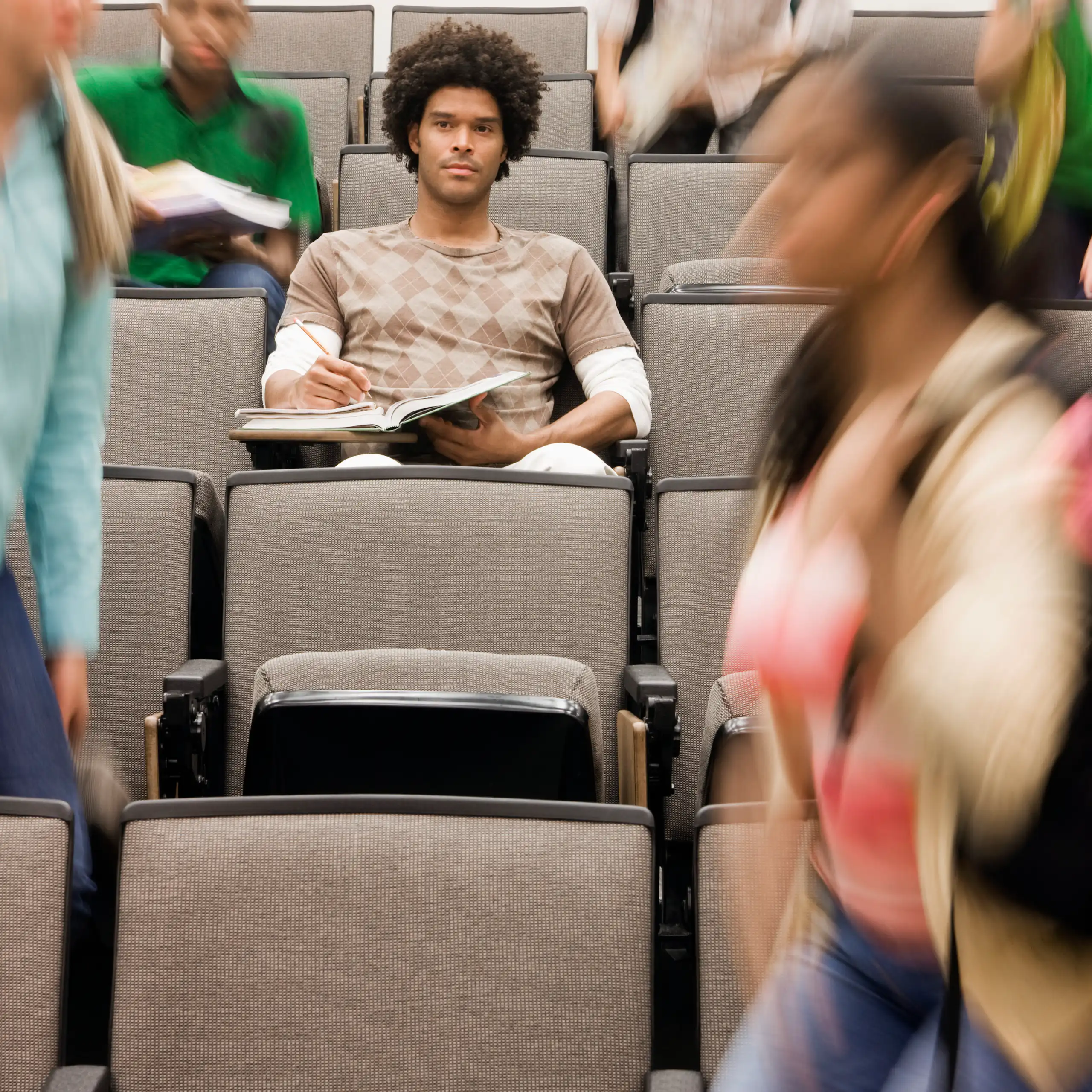 College student sitting in lecture hall while others walk around.