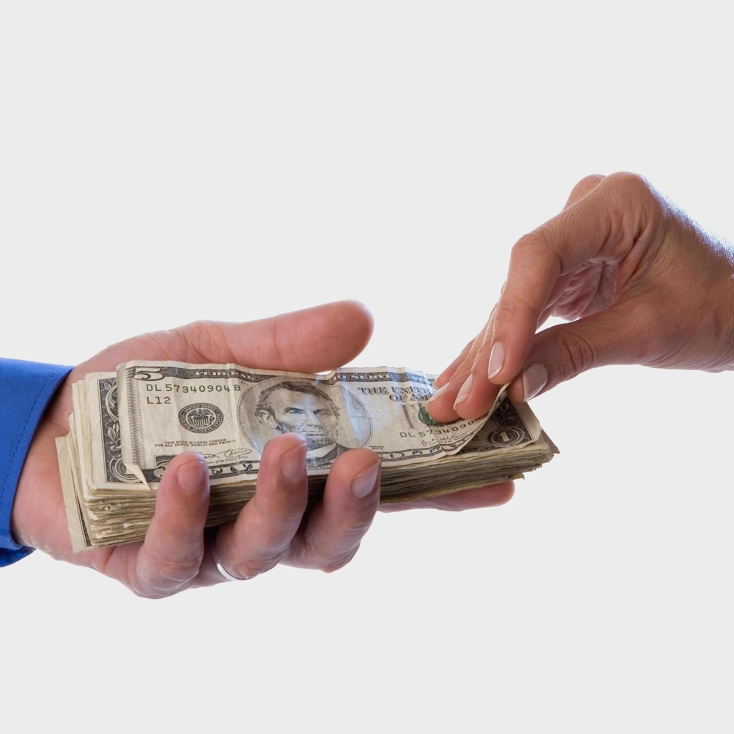 A hand with a blue sleeve holds a stack of USD cash as another hand pulls the top bill from the stack.