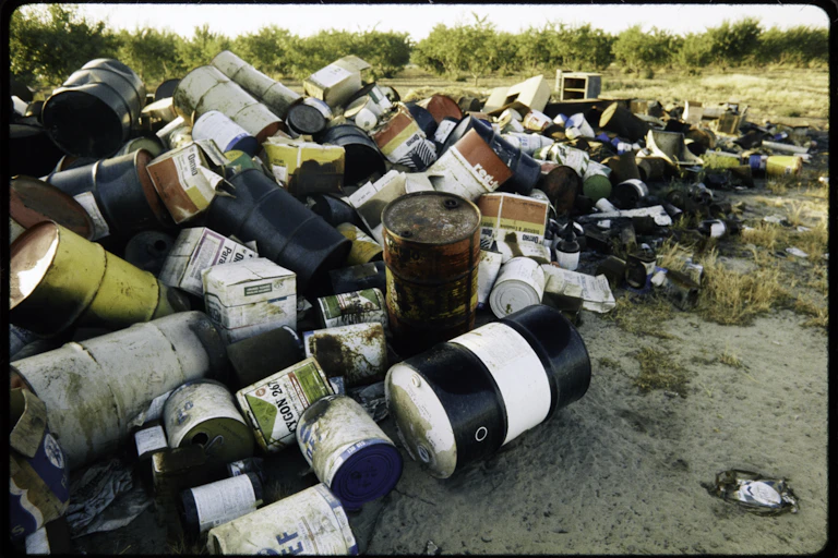 Metal and plastic barrels with various labels on them sit in a pile.