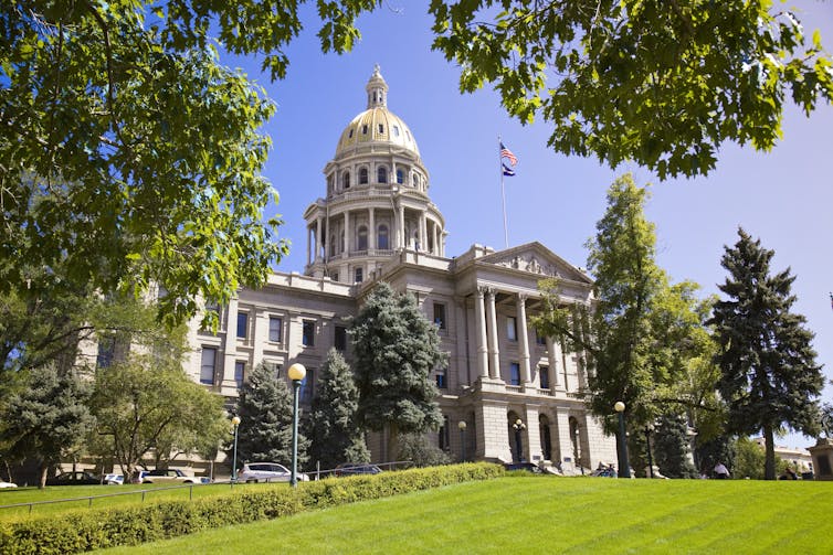 A large building with a gold dome on a sunny day behind a green lawn.