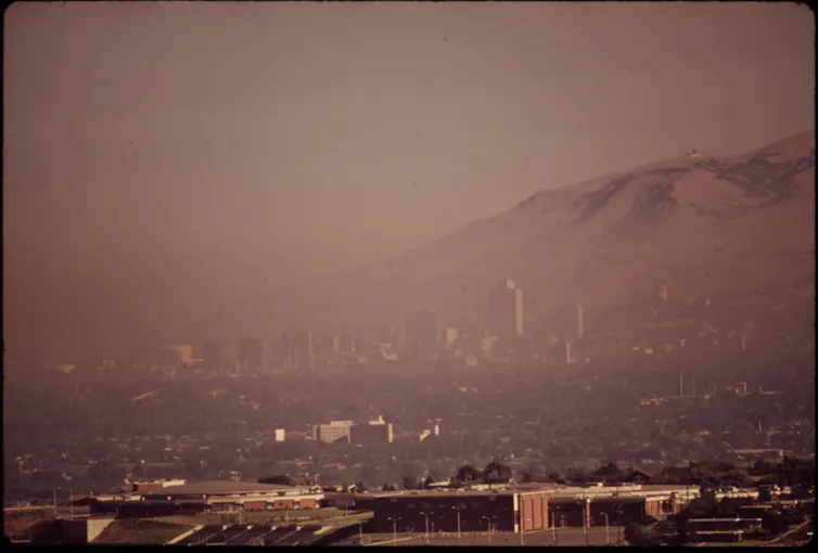 A curtain of smog obstructs the view of a city and the mountains behind it.
