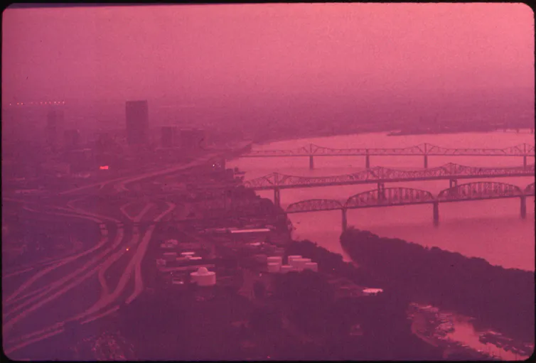 A thick layer of smog covers a cityscape with tall buildings and several bridges over a river.