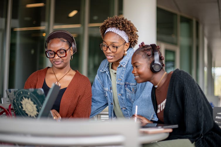Three female college students work together at a computer.