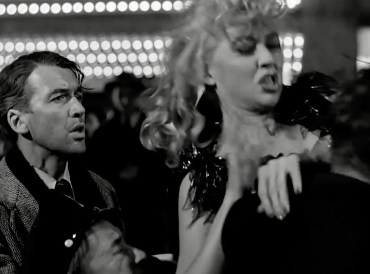 Black-and-white movie still of a young women being dragged away by the police as a worried young man looks on.