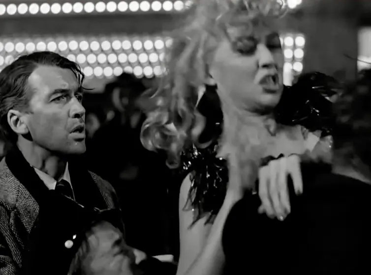 Black-and-white movie still of a young women being dragged away by the police as a worried young man looks on.