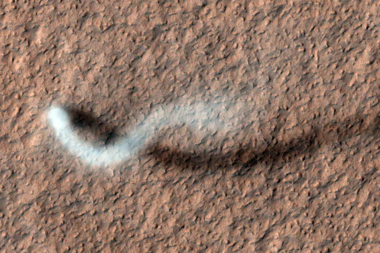 An overhead view of a column of dust snaking across a rocky landscape.