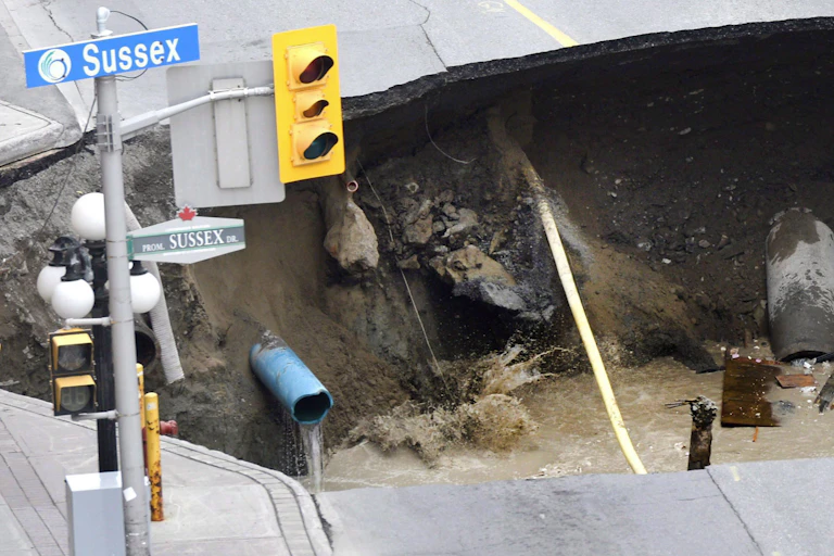 A massive sinkhole on a city street. The streets sign Sussex Drive and a stop light are in the top left of the photo.