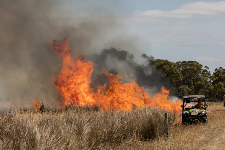 A small firefighting vehicle next to a dry paddock that is in flames.