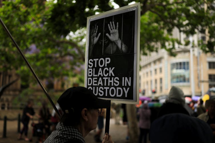 A man holds a protest sign that says stop black deaths in custody