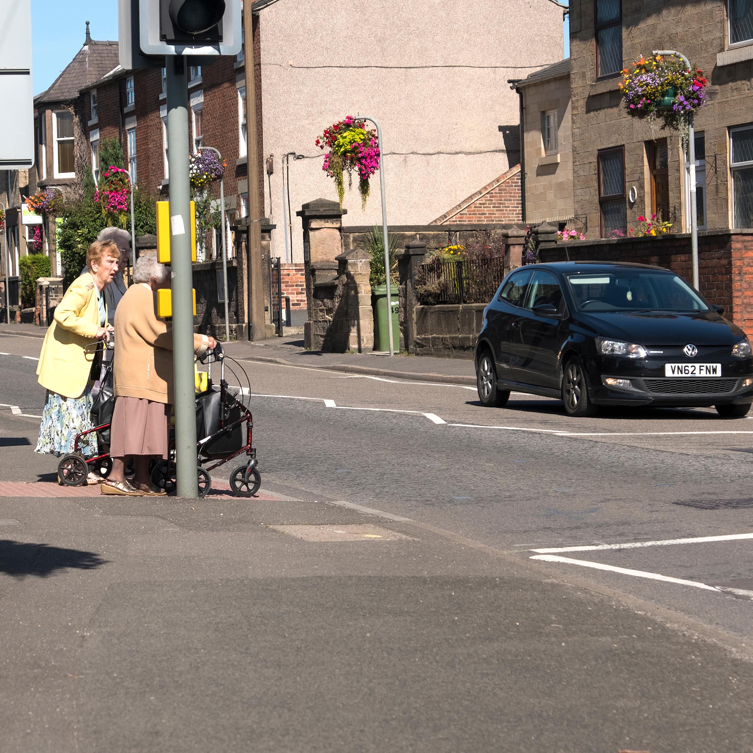 Three older people standing at a pedestrian crossing while a car waits.