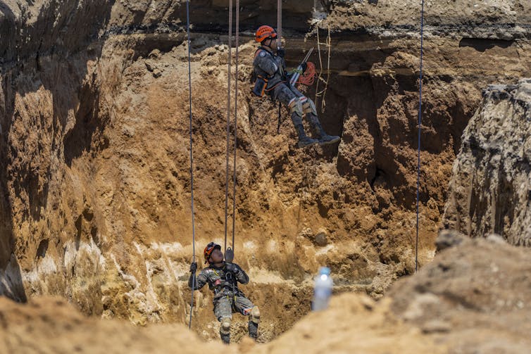 Rescuers descend by ropes into a massive sinkhole.