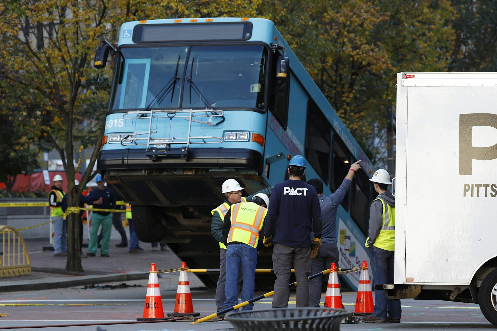 The front of a blue public transit bus pokes out of a sinkhole.